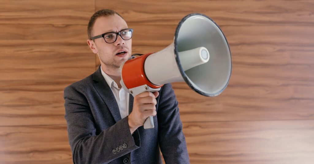 pexels photo 8847006 8847006 Man in suit holding a megaphone, making a public announcement indoors.